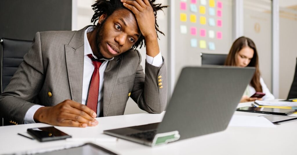 African American man looking stressed in office, with laptop and smartphone on desk. Collins Ero